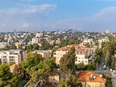 בתים מוקפים בצמחייה, שמיים בהירים עם קצת עננים