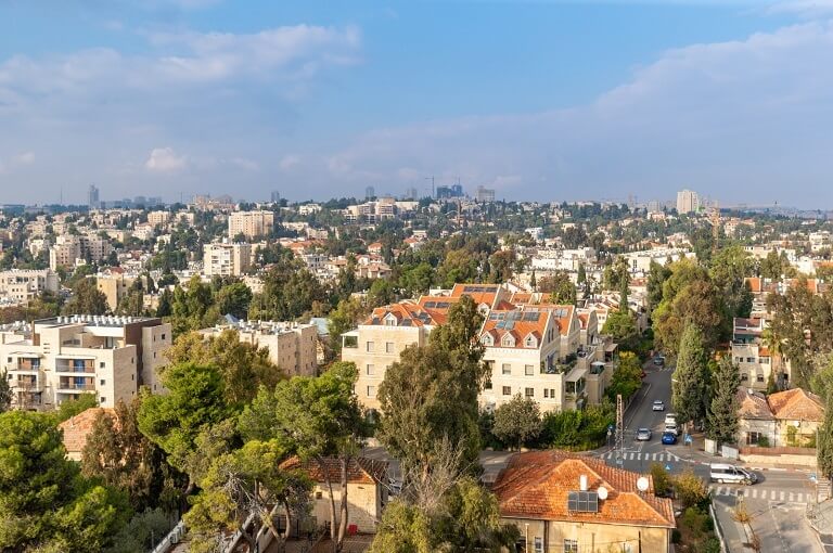 בתים מוקפים בצמחייה, שמיים בהירים עם קצת עננים